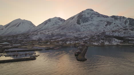 Local-fishing-boat-returns-to-harbour-from-arctic-waters,-sunset-snowy-mountains