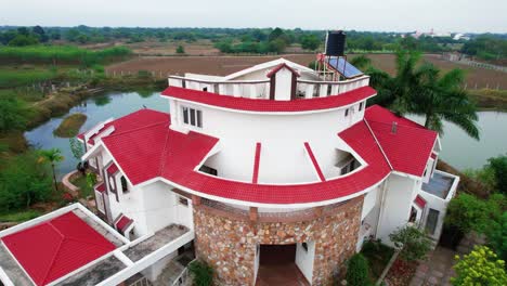 New-brick-red-roof-on-a-three-story-white-house-for-relaxing-vacation-in-Vadorara,-India,-surrounded-by-a-large-lake-with-tropical-forest-and-clear-blue-sky