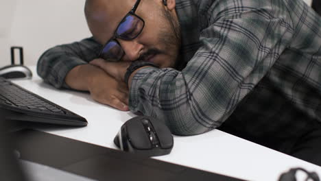 A-young-Indian-entrepreneur-asleep-on-his-arms-slumped-over-a-desk-in-front-of-his-computer,-exhausted-from-working-late-putting-together-his-business-proposal