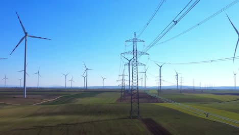 Malerische-Aussicht-Auf-Rotierende-Windkraftanlagen-Und-Strommasten-Vor-Blauem-Himmel-In-Grünen-Feldern