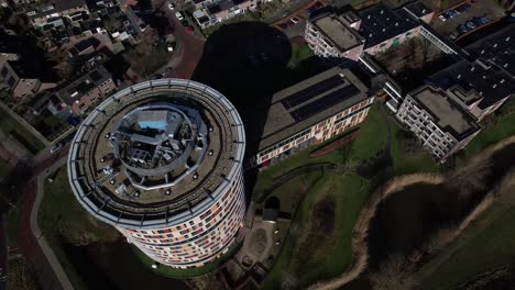 Rotating-pan-and-top-down-aerial-view-of-colorful-round-towering-building-of-service-flat-elderly-residential-home-in-Dutch-tower-town
