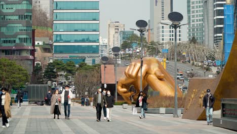 People-In-Masks-Walking-In-The-Street-Passing-By-Gangnam-Style-Statue-In-Seoul,-South-Korea