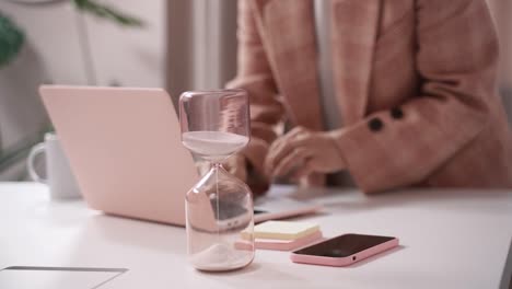 Woman-working-against-the-clock-on-her-laptop,-due-date-deadline-concept,-time-control-with-an-hourglass
