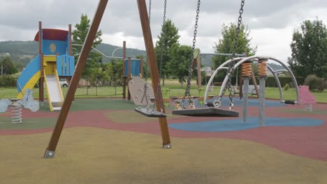Swings-swinging-in-empty-children's-playground-on-gloomy-day
