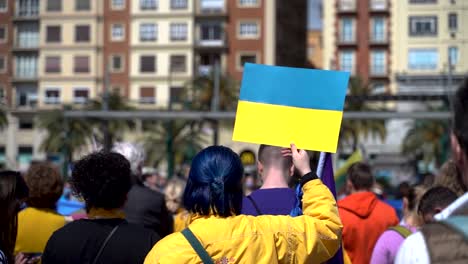Frau-In-Gelb-Mit-Blauen-Haaren-Hält-Bei-Protesten-Die-Ukrainische-Flagge-Hoch