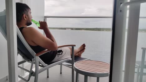 Un-Hombre-Asiático-Tomando-Cerveza-Heineken-Y-Disfrutando-De-Las-Vacaciones-En-Su-Balcón,-Apartamento-Cerca-De-Un-Fondo-De-Video-Del-Océano-En-4k