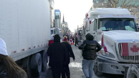 Gente-De-Protesta-Por-La-Libertad-Caminando-A-Través-De-Un-Convoy-De-Camiones-En-Canadá