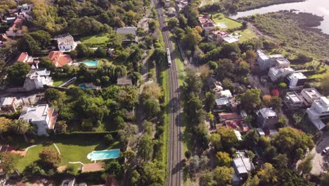 Aerial-drone-tracking-shot-of-small-train-crossing-suburb-of-Buenos-Aires-in-Argentina