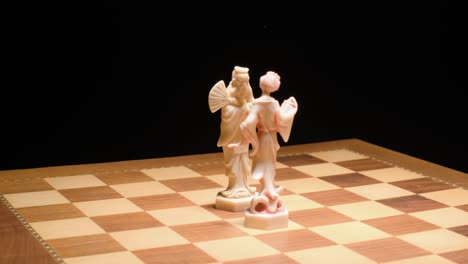 Tracking-motion-King-and-Queen-ivory-pieces-on-Chessboard,-Black-Background