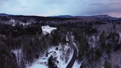 Drone-flies-along-winding-road-in-snowy-mountains-of-Vermont-during-sunset