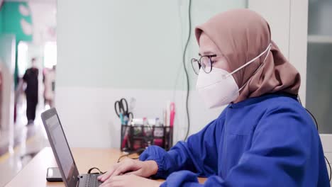 Young-Asia-lady-doctor-in-blue-medical-uniform-with-hijab-using-computer-laptop-talking-video-conference-call-with-patient-at-desk-in-health-clinic-or-hospital