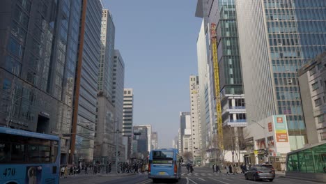 Geschäftiges-Städtisches-Straßenleben-Mit-Fußgängern,-Die-Die-Straße-Mit-Bussen-überqueren,-Und-Verkehr-Tagsüber