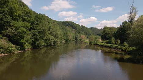 Lush,-green-nature-surrounding-a-calm,-brown-river-in-North-Rhine-Westphalia,-Germany-on-a-sunny-summer-day