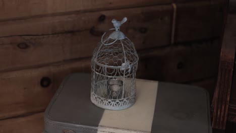 Bird-cage-candle-sitting-on-a-decorative-suitcase-table-at-a-wedding-reception