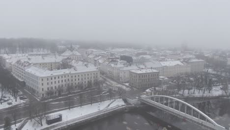 Drone-shot-of-pedestrian-arch-bridge-over-Emajõgi-river,-Tartu-city-covered-with-mist