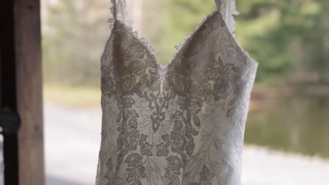 Wunderschönes-Hochzeitskleid,-Das-An-Einer-Holzkonstruktion-Vor-Einem-Hochzeitsort-Hängt,-Mit-Bokeh-Von-Bäumen-Im-Hintergrund