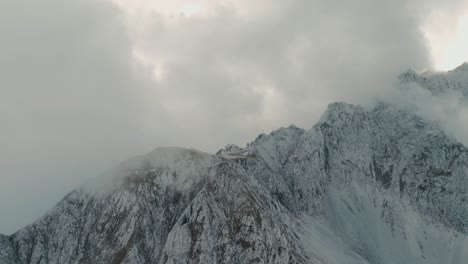 Volando-A-Través-De-Las-Nubes-Y-La-Niebla-Revelando-La-Cima-De-La-Montaña-De-Los-Alpes-De-La-Cadena-Norte-En-Austria-Y-La-Cabaña-Cubierta-Rodeada-De-Nubes