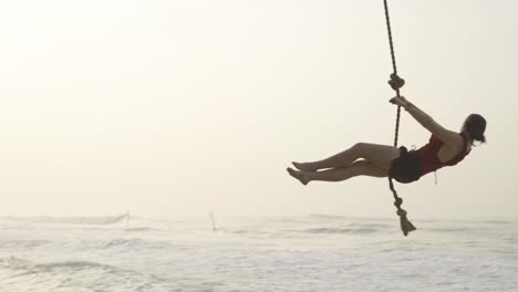 Woman-swings-from-palm-tree-over-ocean-during-sunrise-on-paradise-beach