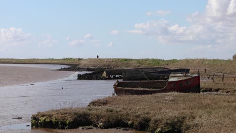 Boat-Wreck-on-the-shore-at-Orford-on-the-Suffolk-Coastline,-United-Kingdom,-with-Figure-walking-away-in-the-distance