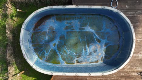 Top-down-rising-aerial-of-an-empty-and-dirty-above-ground-pool