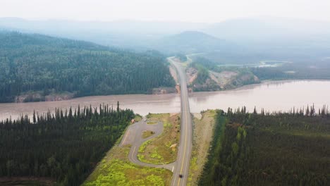 Aerial-drone-shot-flying-high-over-a-bridge-surrounded-by-dense-coniferous-forest-with-the-view-of-a-camping-site-close-beside-Alaskan-Highway-in-USA-at-daytime