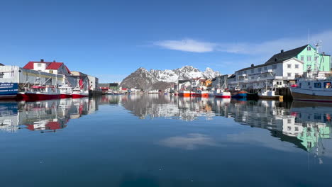 Static-shot-of-Henningsvaer-Harbor-with-Buildings-and-boats-reflecting-on-the-water-surface,-scenic-mountain-in-the-background,-Lofoten-Island