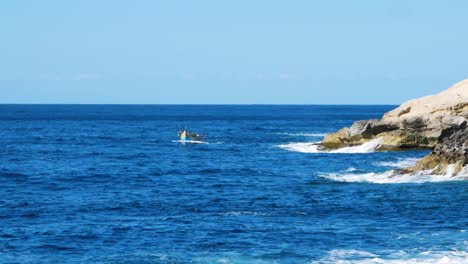 Local-Maltese-man-sailing-near-rocky-coastline-while-waves-hitting-stone