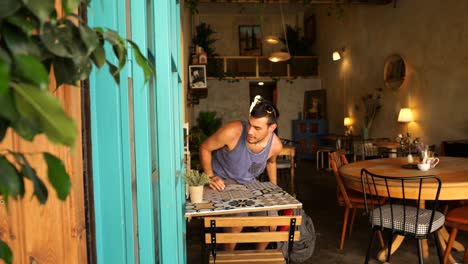 Caucasian-Male-Tourist-Taking-Backpack-Off-Before-Sitting-Down-At-Cafe-Table-In-Nicosia