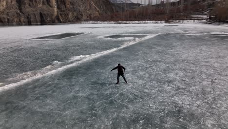 Aerial-Over-Silhouette-Of-Adult-Male-Learning-To-Ice-Skate-On-Frozen-Khalti-Lake-At-Ghizer-Valley