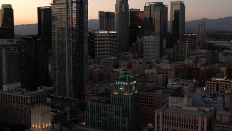 Establishing-aerial-view-of-downtown-Los-Angeles-at-sunset,-Eastern-Columbia-building-with-skyscraper-buildings-behind