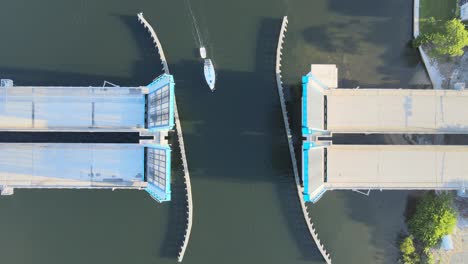 Aerial-view-of-boats,-including-a-sail-boat,-passing-through-an-open-drawbridge