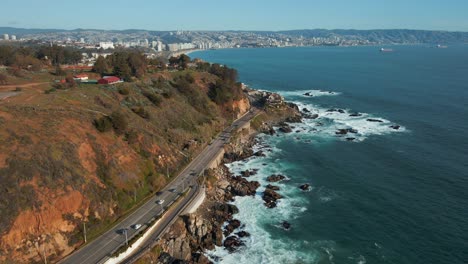 Aerial-view-following-Avenida-Borgoño-waterfront-coastal-road-alongside-Reñaca-affluent-ocean-waves