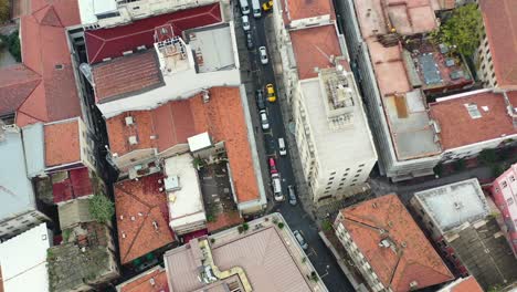 Aerial-top-down-view-of-cars-driving-down-a-narrow-alley-street-surrounded-by-tall-European-residential-buildings-in-downtown-Istanbul-Turkey