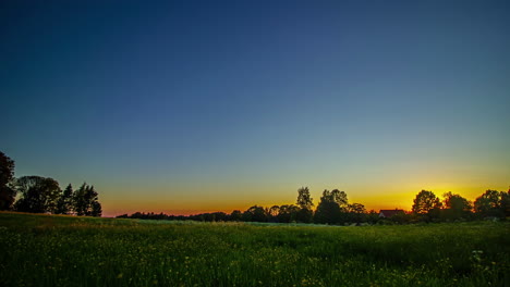 Timelapse-shot-of-beautiful-sunset-over-green-grasslands-with-the-view-of-cottage-in-background-at-dusk
