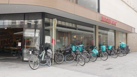 Lone-Deliveroo-rider-and-multiple-bikes-parked-outside-Burger-King-waiting-for-food-orders-to-deliver---Brussels,-Belgium