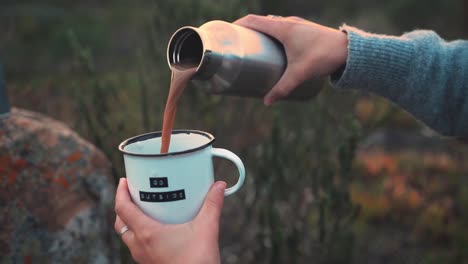 Slow-motion-footage-of-a-woman-pouring-a-cup-of-hot-chocolate-while-camping