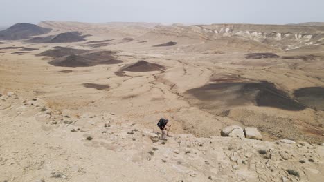 One-man-hiker-trekking-along-the-edge-of-Ramon-Crater,-Negev-desert,-Israel---aerial-orbit-view