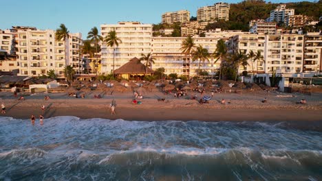 tropical-Mexican-beach-town-at-sunset-with-tourists-in-Puerto-Vallarta-Mexico,-aerial
