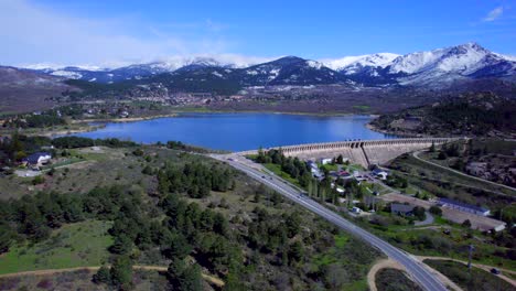 Panoramic-aerial-view-over-the-Navacerrada-Reservoir-with-the-beautiful-snow-capped-mountains-on-the-horizon