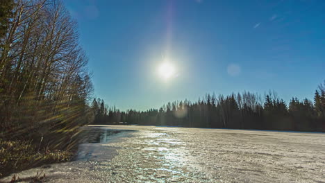 Close-up-shot-over-snow-melting-of-lake-surrounded-by-forest-on-all-sides-with-sun-movement-in-timelapse-throughout-the-day-in-rural-countryside