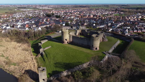 An-aerial-view-of-Rhuddlan-Castle-on-a-sunny-spring-morning,-flying-right-to-left-around-the-castle-with-the-town-of-Rhuddlan-in-the-background,-Denbighshire,-Wales,-UK