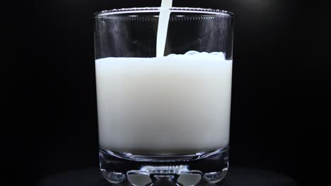 Pouring-Fresh-Milk-Into-Clear-Glass-In-Black-Background