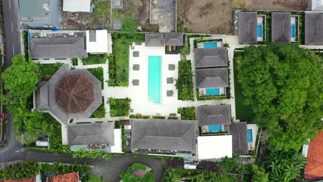 Motorbikes-driving-by-a-pool-villa-complex-and-construction-site-in-Umalas-Bali,-aerial-top-down
