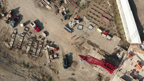 Aerial-top-down,-workers-walking-on-construction-site-foundation-with-crawler-crane
