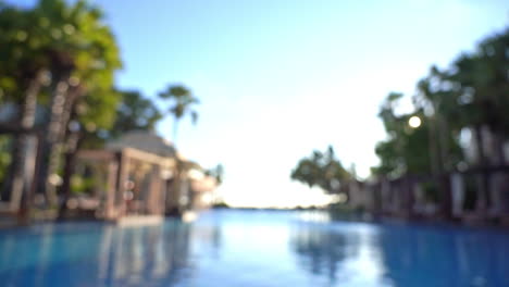 Blurred-view-from-inside-hotel's-outroor-lounge-swimming-pool-with-tropical-palms-and-rest-area