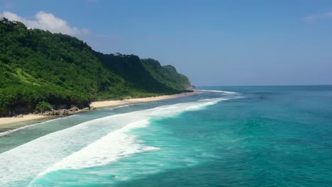 tropical-turquoise-blue-ocean-waves-along-mountain-coastline-beach-of-Nyang-Nyang-in-Uluwatu-Bali-on-sunny-day,-aerial