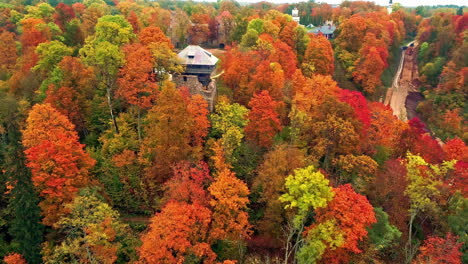 Aerial-drone-shot-surrounded-by-colorful-bright-yellow-orange-and-green-trees-in-autumnal-forests-with-the-view-of-of-an-old-medieval-building-on-a-cloudy-day