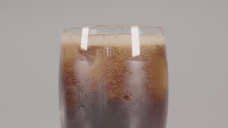 Ice-cubes-dropping-into-glass-of-cola-and-the-surface-of-the-drink-foams---against-a-white-studio-background