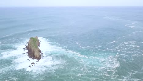 Aerial-shot-of-Rocky-Island-Billano-Irla-with-crashing-waves-in-the-ocean