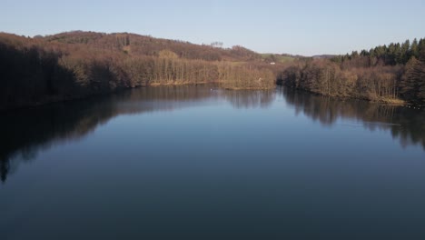Blue-fresh-water-lake-within-a-brown-leafless-forest-on-a-bluebird-day-in-Germany